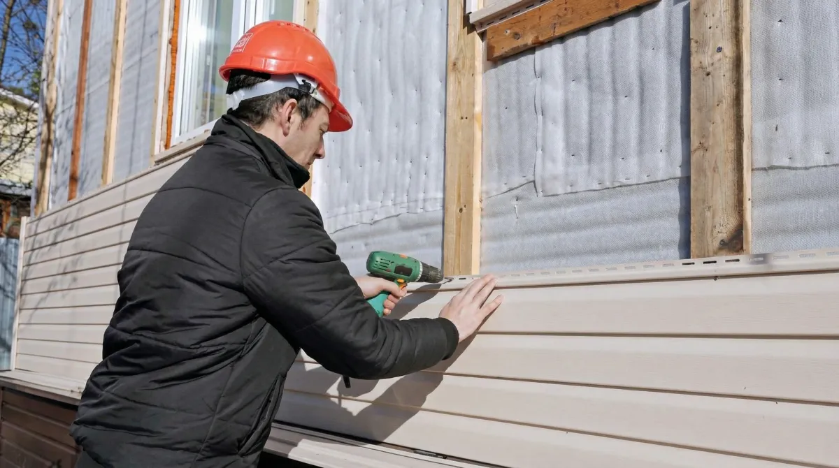 Siding replacement professional using a power drill to install new tan vinyl siding on a home exterior in Denver, CO